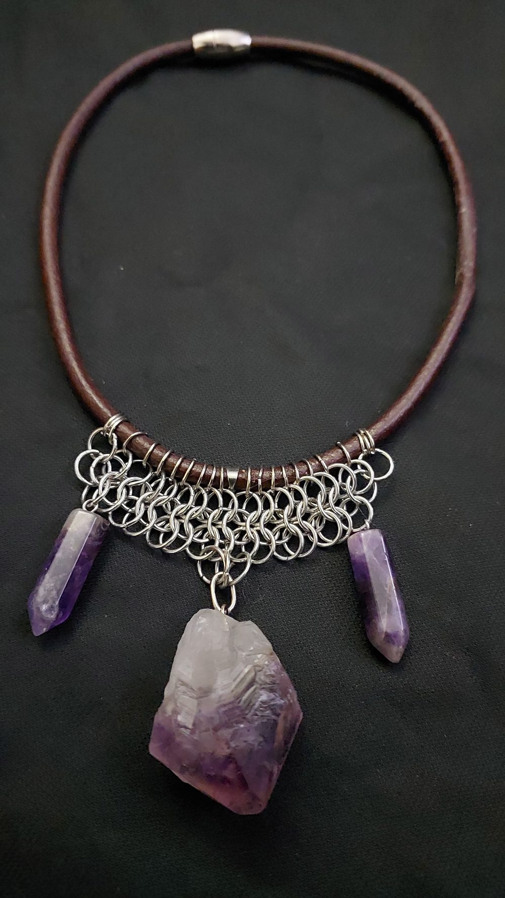 Detalle de malla de argollas metálicas sobre cinta, con puntas de amatista